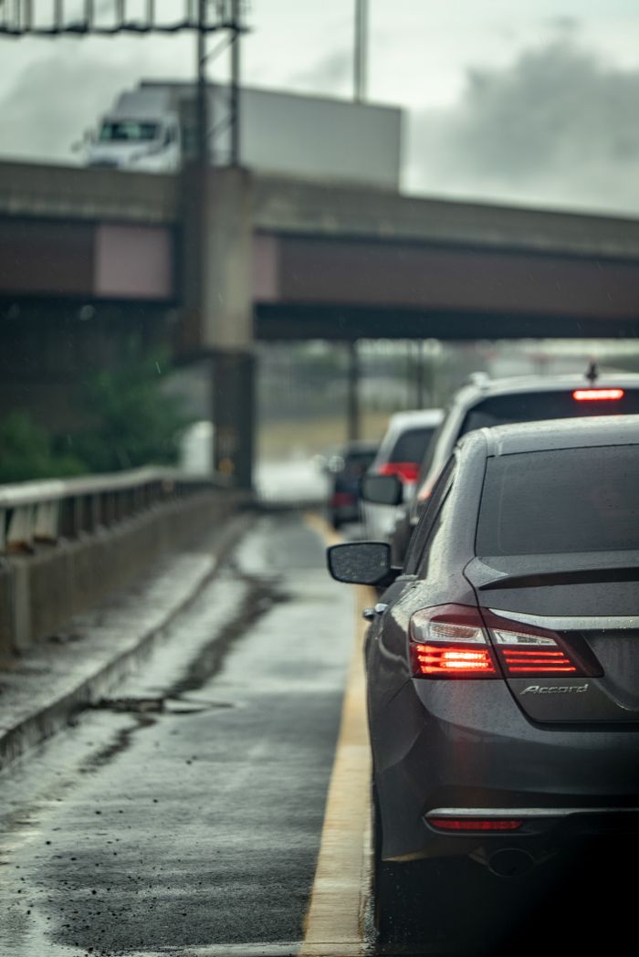 Home Cars stuck in traffic on a wet highway under an overpass during a rainy day, highlighting urban congestion.